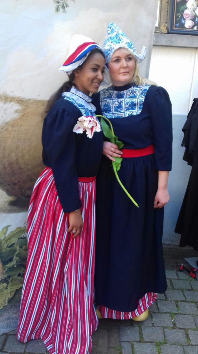 Twee deelneemsters in Nederlandse klederdracht met een tulp tussen hen in