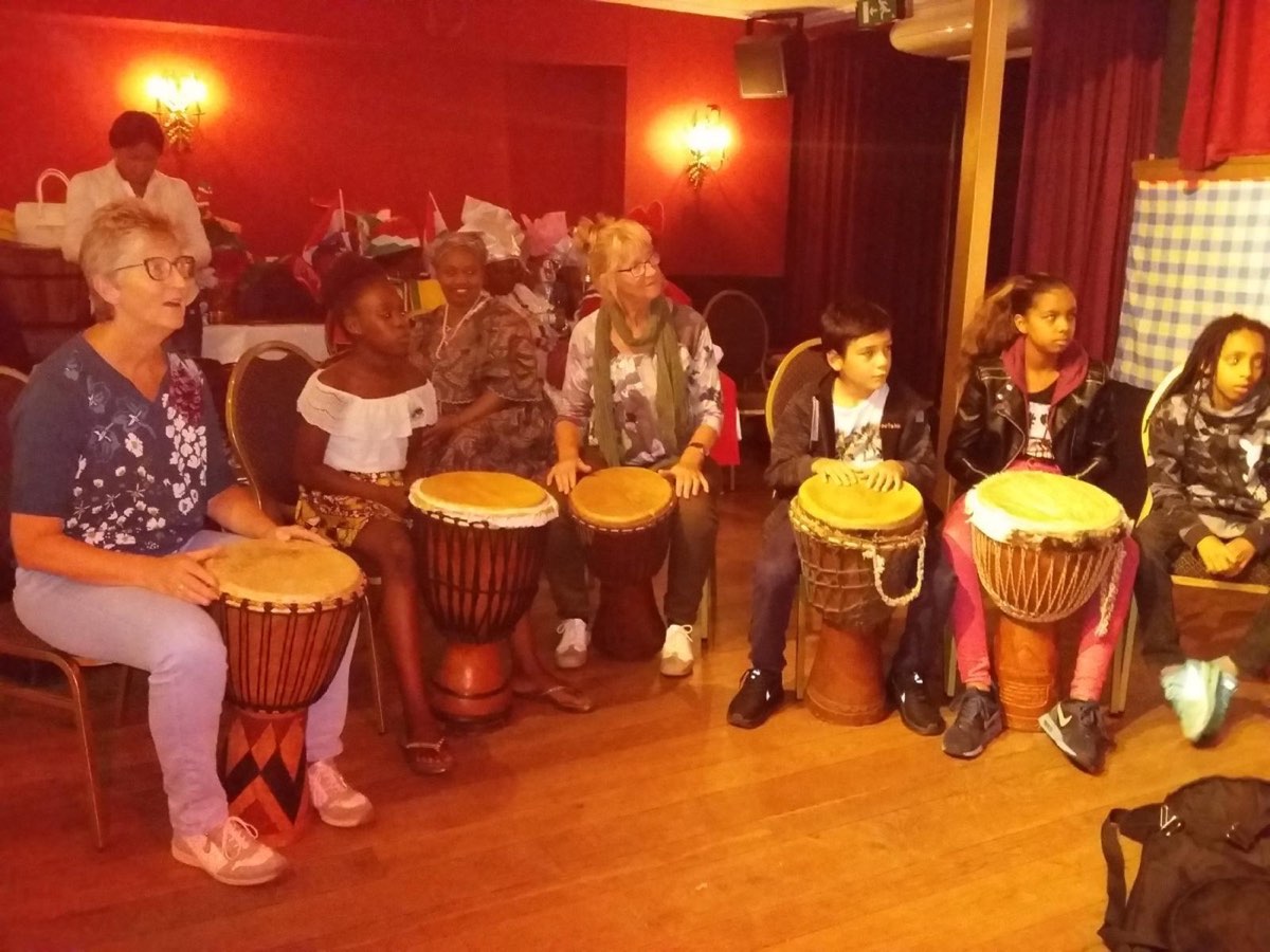 Kinderen en volwassenen in een kring achter djembés tijdens de workshop