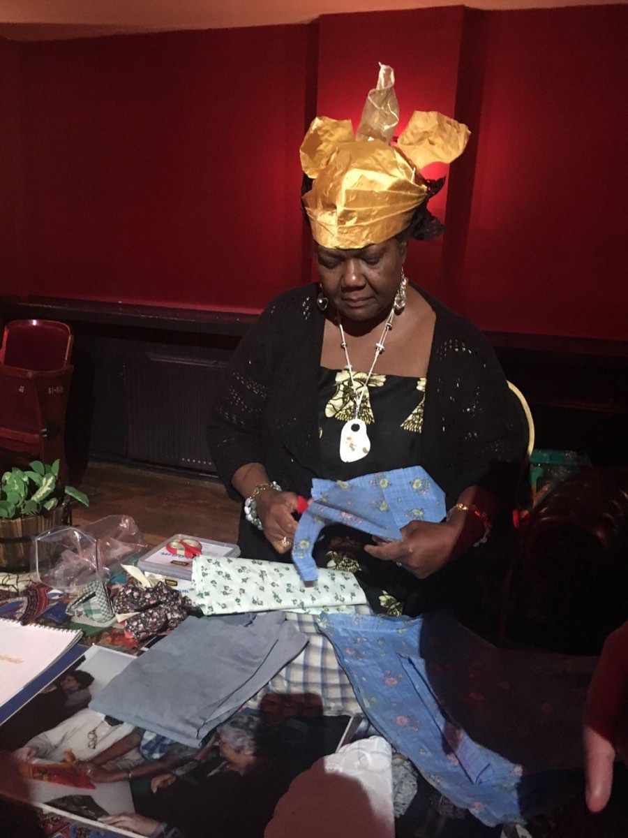 Vrouw met gouden angisa bekijkt historische stoffen aan een tafel vol foto’s