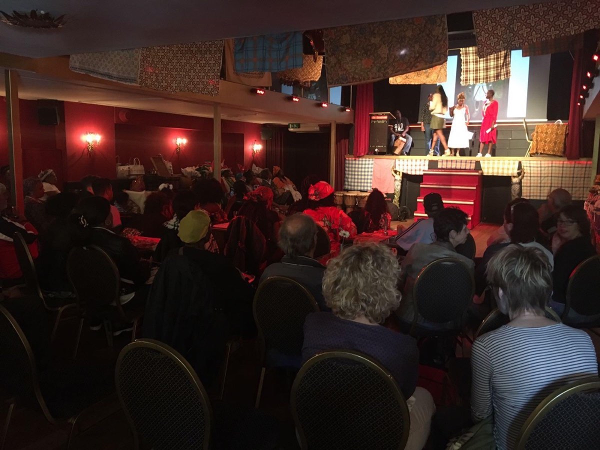 Een volle zaal kijkt naar het podium, met doeken aan het plafond