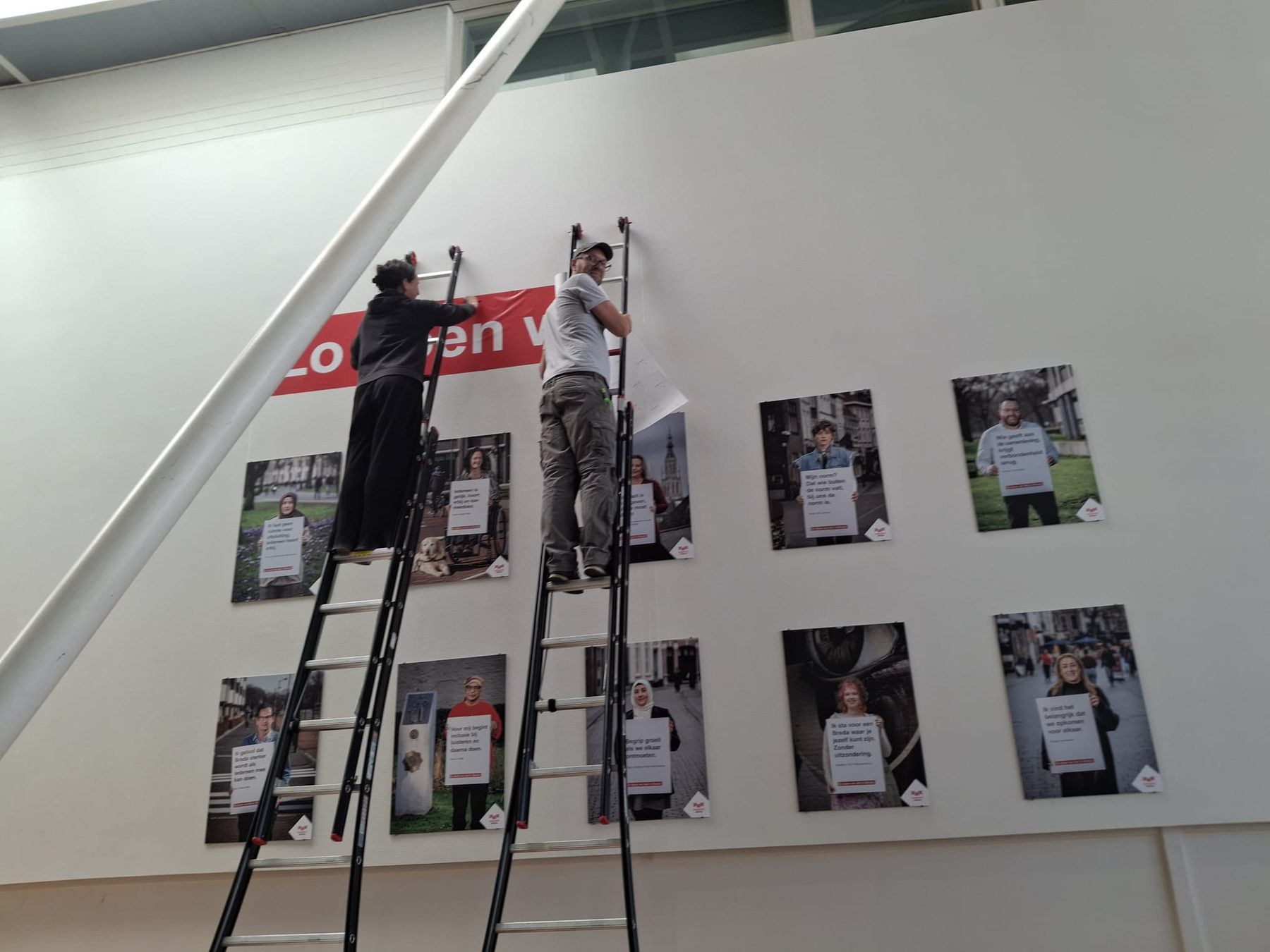 Twee mensen op ladders hangen de portretten van de expositie ‘Zo doen we dat in Breda’ op in de Nieuwe Veste